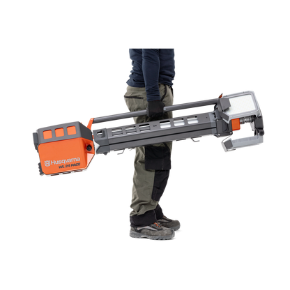 Person carrying a Husqvarna construction product, possibly a drill or cutter, in a studio setting.